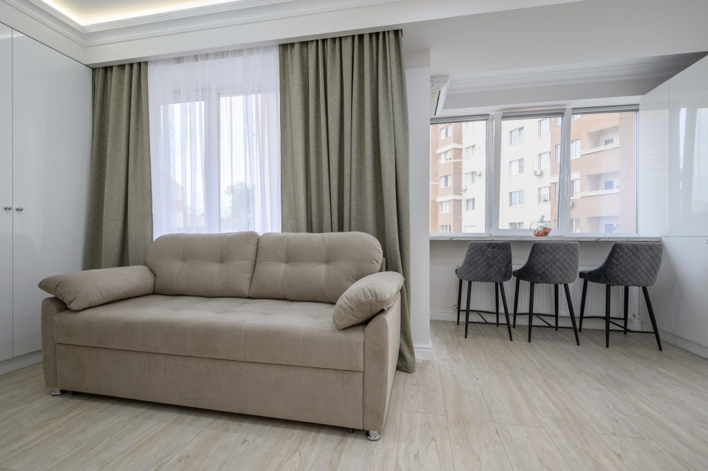 Small studio flat living room with a couch and a dining counter with chairs at windowsill